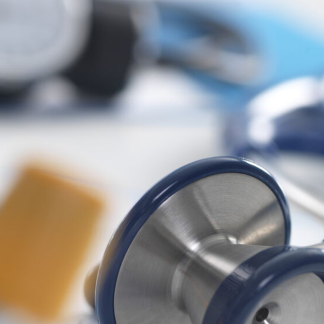 A close-up of a stethoscope with medical supplies in the background.