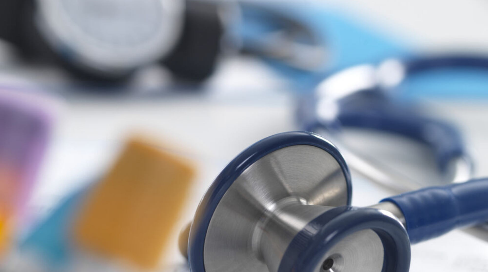 A close-up of a stethoscope with medical supplies in the background.