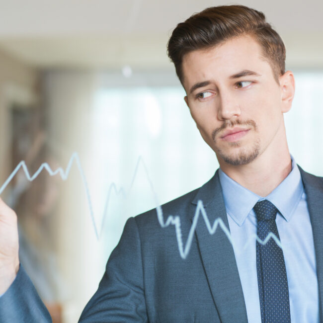 Businessman in a suit drawing a fluctuating financial line graph on transparent glass, illustrating investment analysis.