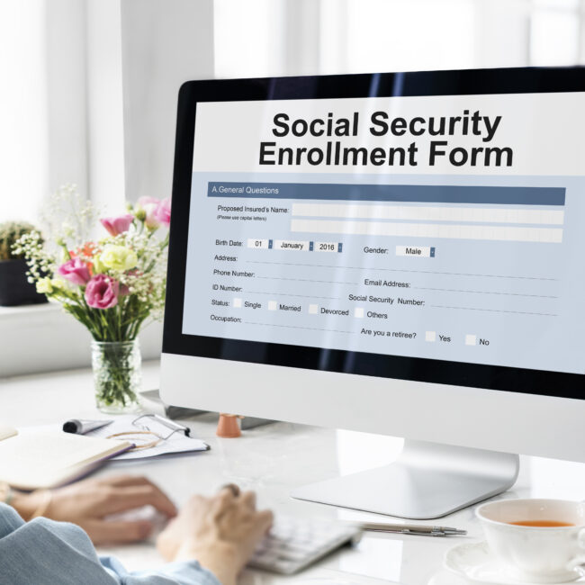 Person using a computer displaying a Social Security enrollment form while reviewing retirement benefit information.