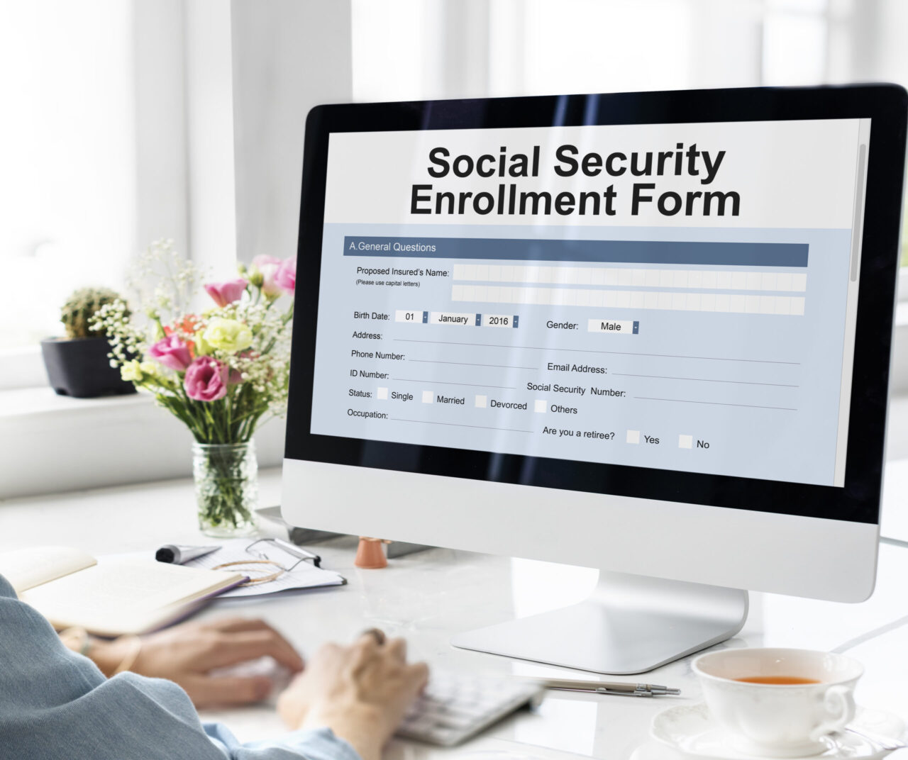 Person using a computer displaying a Social Security enrollment form while reviewing retirement benefit information.