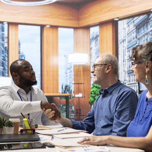 Financial broker shaking hands in agreement with senior man Financial broker shaking hands in agreement with senior man, ensuring a partnership to help them secure their future and retirement plans. Meeting in modern office for guidance.
