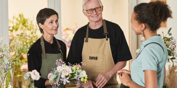 Waist up portrait of two florists talking to customer in flower shop, copy space